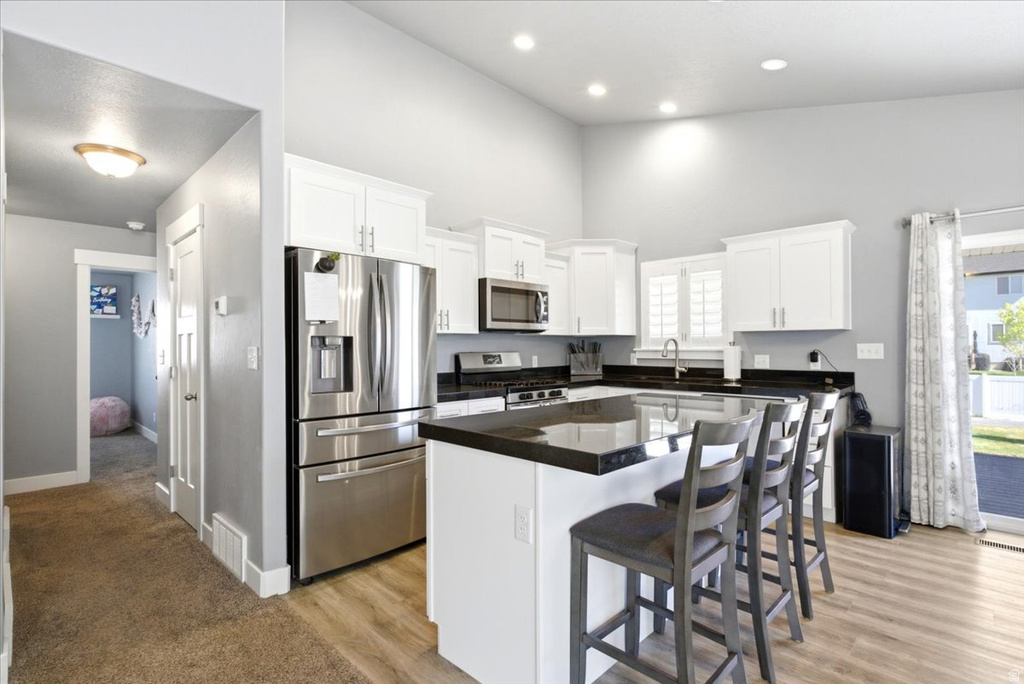 Modern kitchen featuring white cabinetry, stainless steel appliances, dark countertops, a central island with seating, and wood-finish flooring