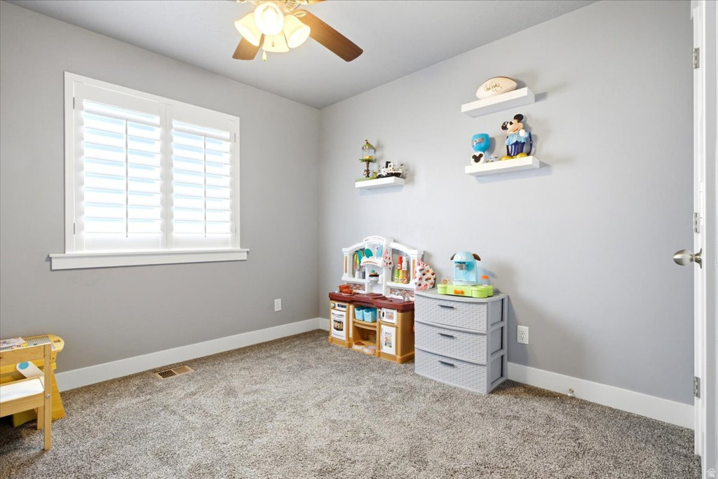 Carpeted room featuring a ceiling fan with light fixture, white window shutters, white trim, and light gray walls