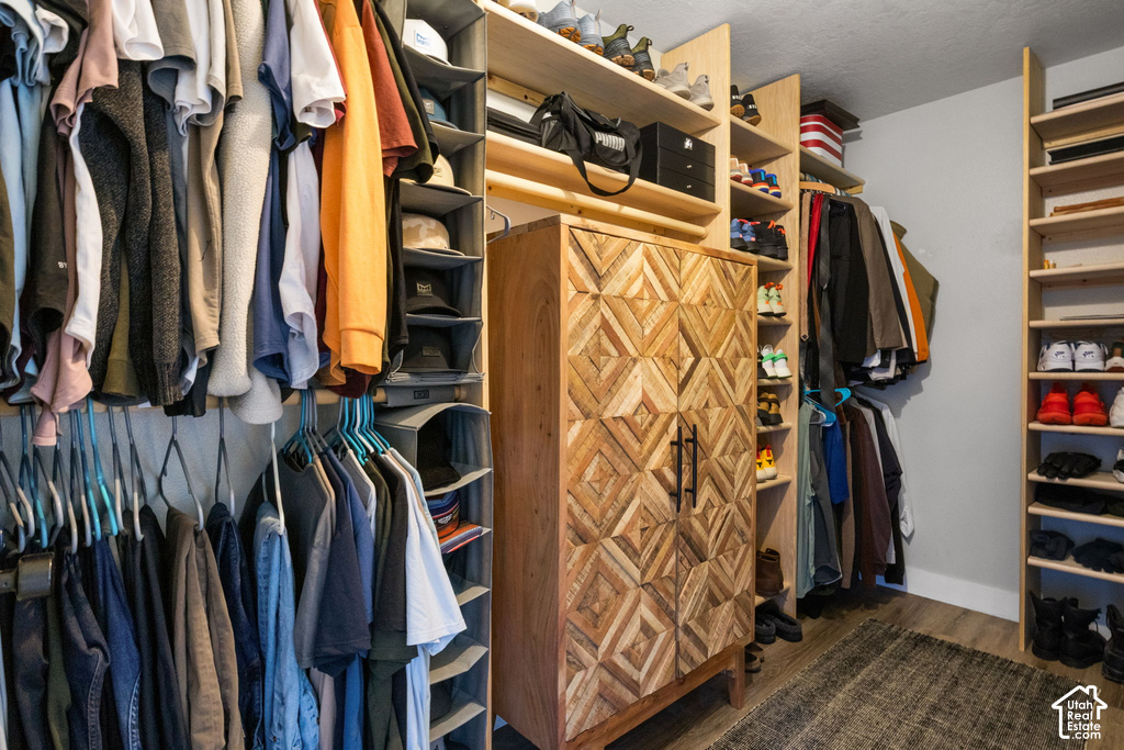 Custom-built closet system featuring extensive shelving, multiple hanging rods, a central wood-finish storage cabinet with geometric door panels, and durable wood-finish flooring