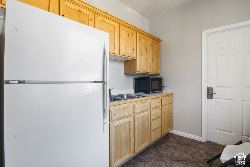 Full-size refrigerator, wood-finish cabinetry, dual-basin stainless steel sink, solid surface countertop, and durable tile flooring