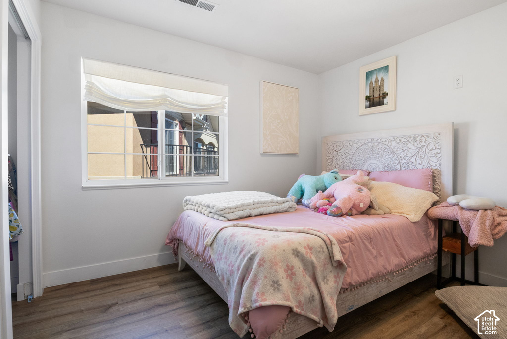 Bright room featuring wood-finish flooring, a white-framed window with a roman shade, and a carved wooden headboard