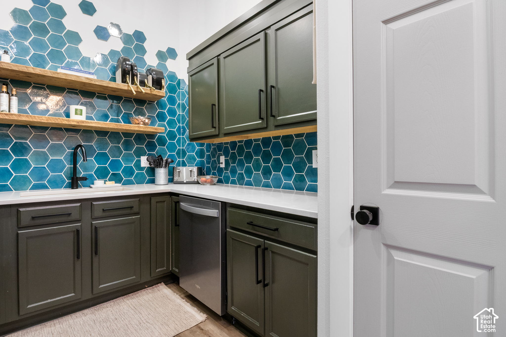 Kitchenette with a vibrant blue hexagonal tile backsplash, dark green cabinetry, white countertops, and a stainless steel dishwasher