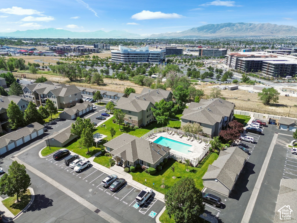 Community grounds featuring multiple residential buildings, a rectangular swimming pool with surrounding lounge chairs, paved parking areas, and detached garages