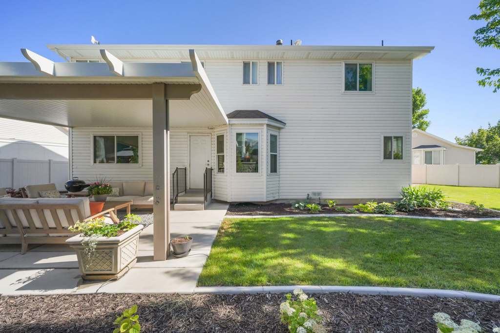 Expansive backyard featuring a covered patio, concrete walkway, vibrant green lawn, and surrounding landscaping