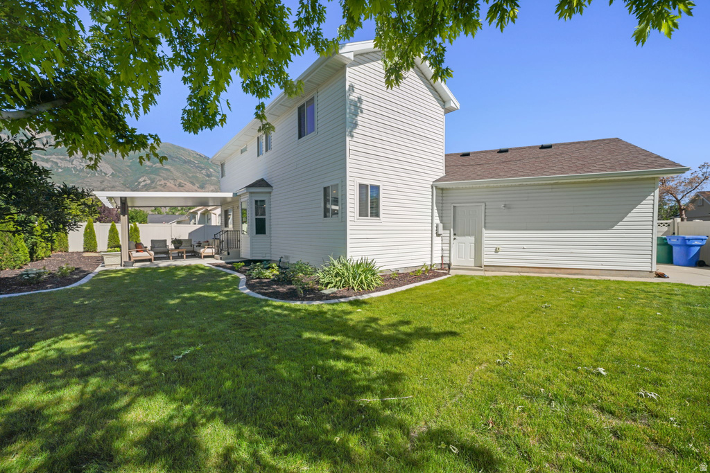 Spacious backyard featuring a manicured lawn, established landscaping beds, and a covered patio structure