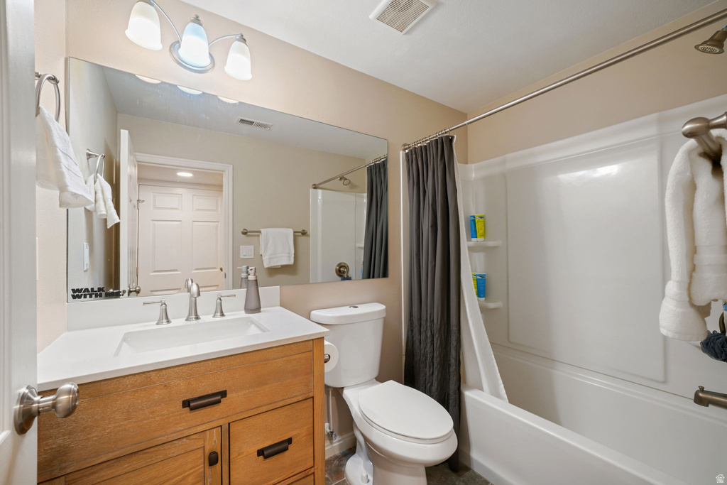 Bathroom featuring a wood-finish vanity with a white countertop and integrated sink, a large wall-mounted mirror, a three-light vanity fixture, a white toilet, and a combination shower/tub with a white surround