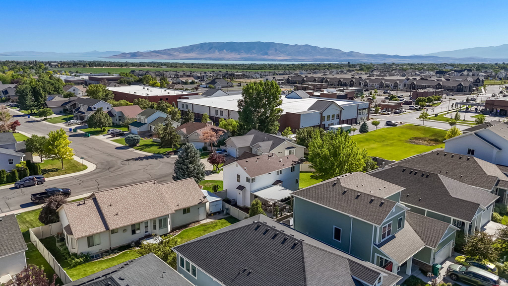 Aerial perspective showcasing a residential neighborhood with diverse architectural styles, a prominent mountain range in the background, a large body of water, and nearby commercial structures