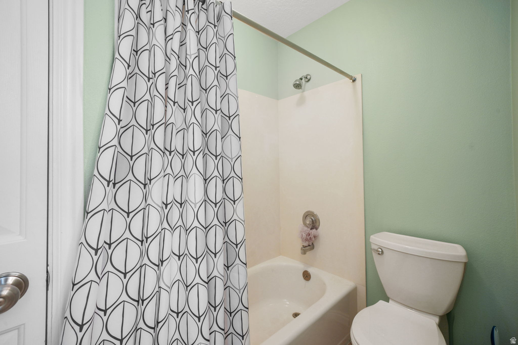 Bathroom featuring a white tub, chrome shower fixtures, a toilet, and light green walls