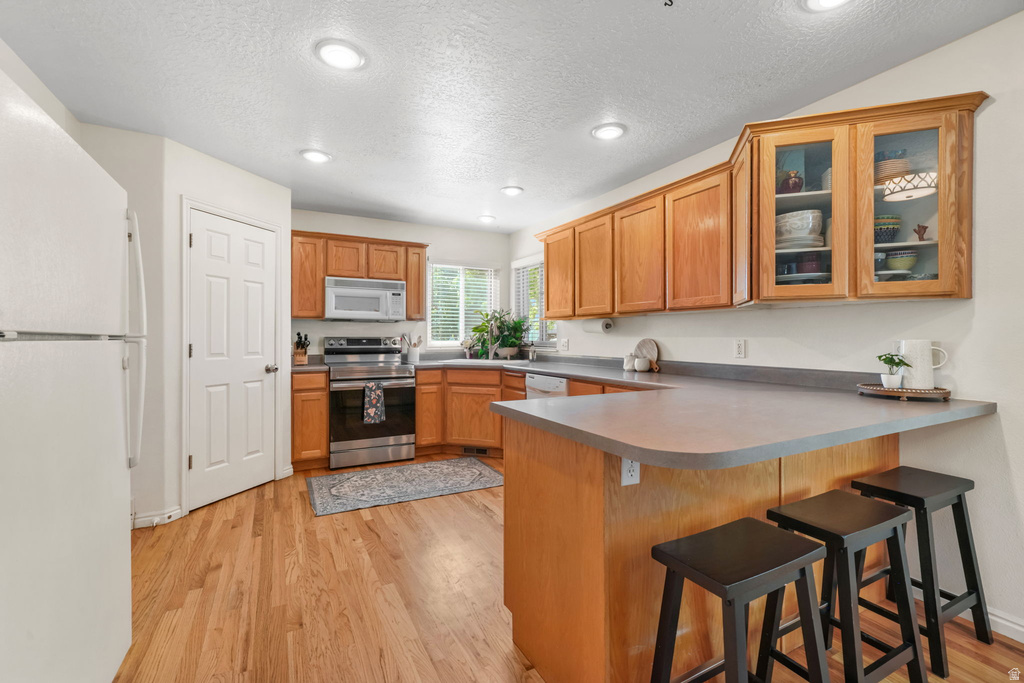 Kitchen featuring wood-finish flooring, recessed lighting, wood cabinetry, stainless steel appliances, and a peninsula with countertop seating