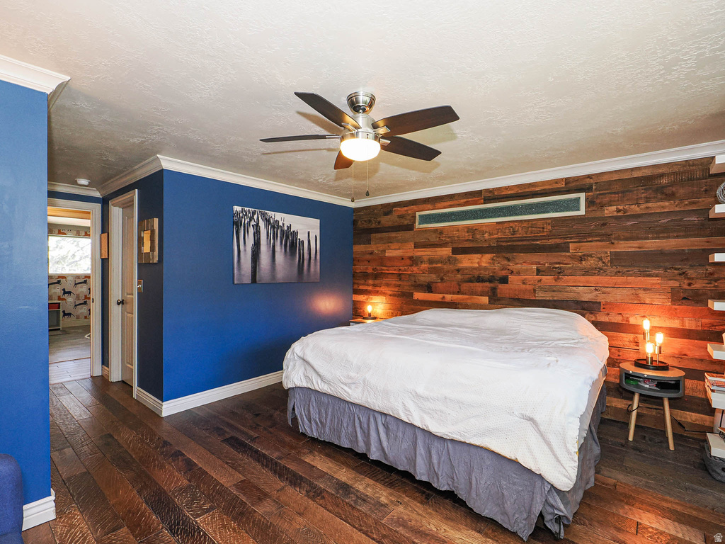 Bedroom featuring wood-finish flooring, a wood-paneled accent wall, and a ceiling fan with integrated lighting