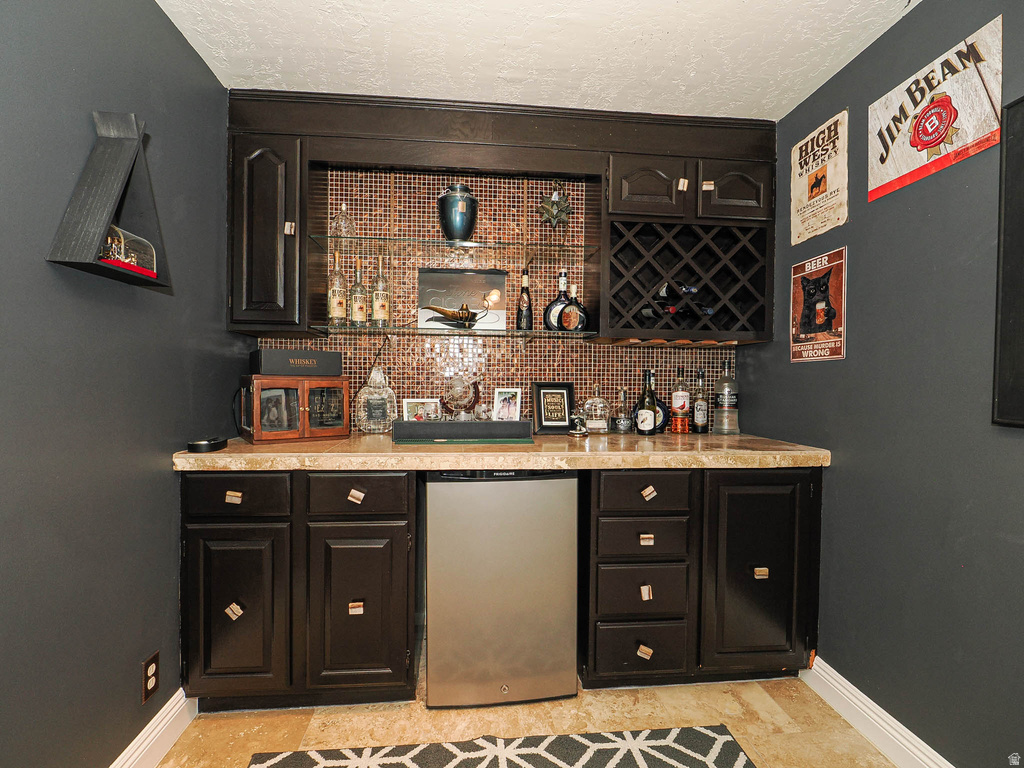 Built-in wet bar featuring dark cabinetry, a mini-refrigerator, and a tiled backsplash