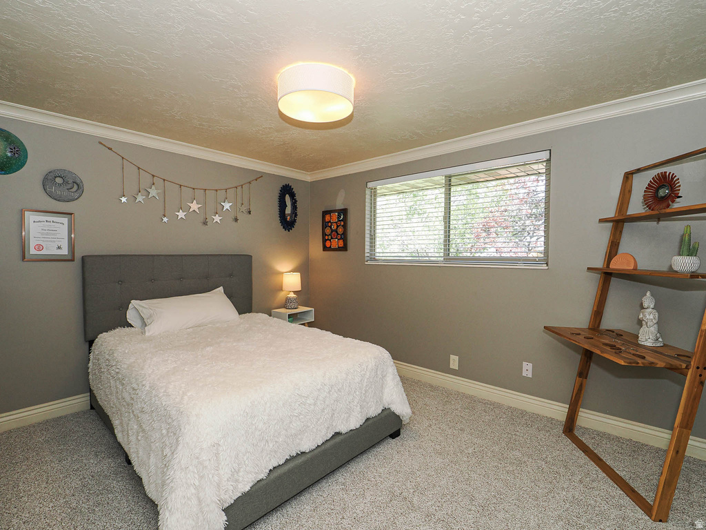 Bedroom featuring a large window with blinds, light-colored carpet flooring, crown molding, and a flush-mount ceiling light fixture