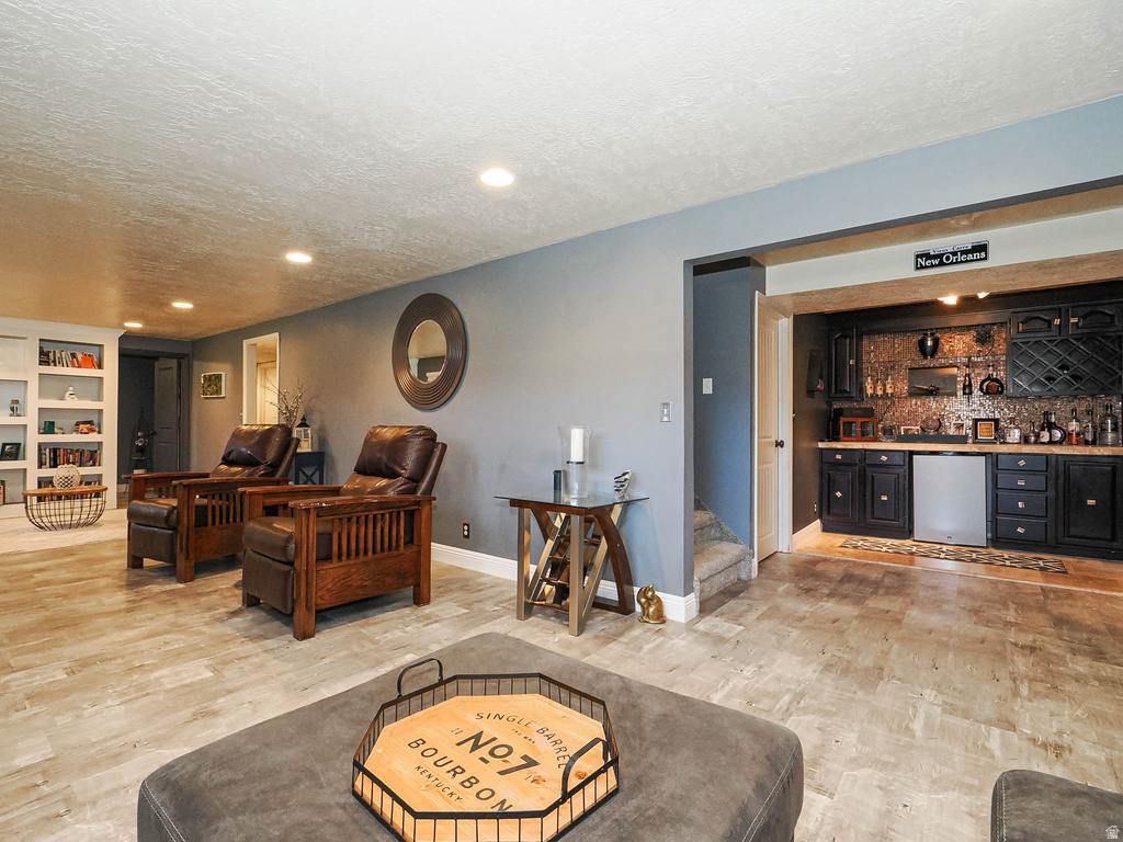 Entertainment area featuring wood-finish flooring, recessed lighting, and a built-in wet bar with dark cabinetry and a beverage cooler