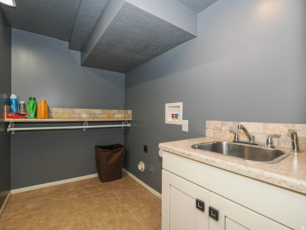 Laundry space featuring a utility sink with a stone-look countertop, integrated cabinetry, tile flooring, a built-in wall shelf, and a hanging rod