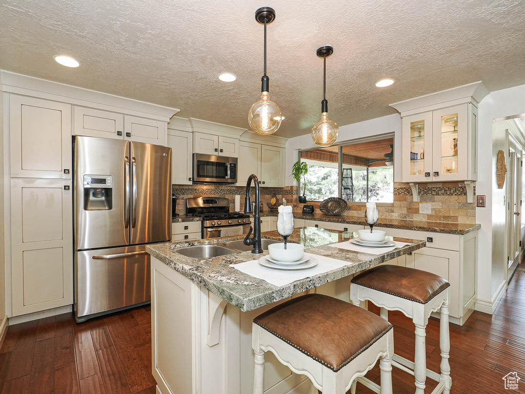 Kitchen featuring a central island with a double basin sink, stone-finish countertops, and dual pendant lighting