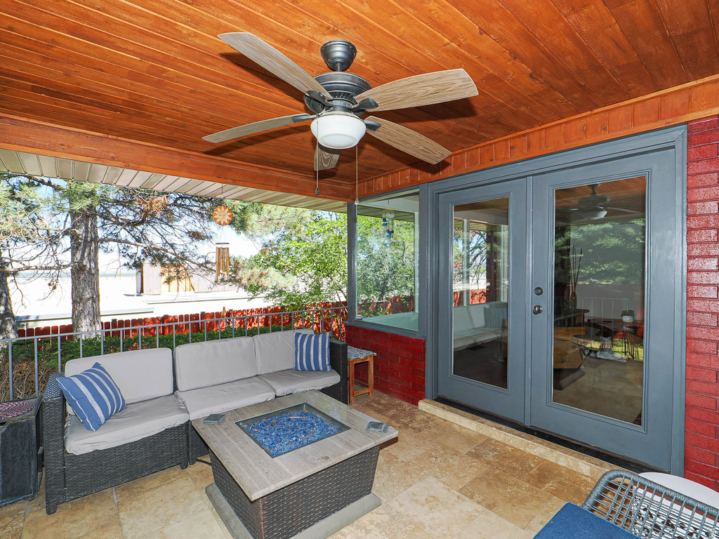 Covered outdoor patio featuring a wood-panel ceiling with a ceiling fan, stone-tile flooring, and full-light double doors with a dark gray finish