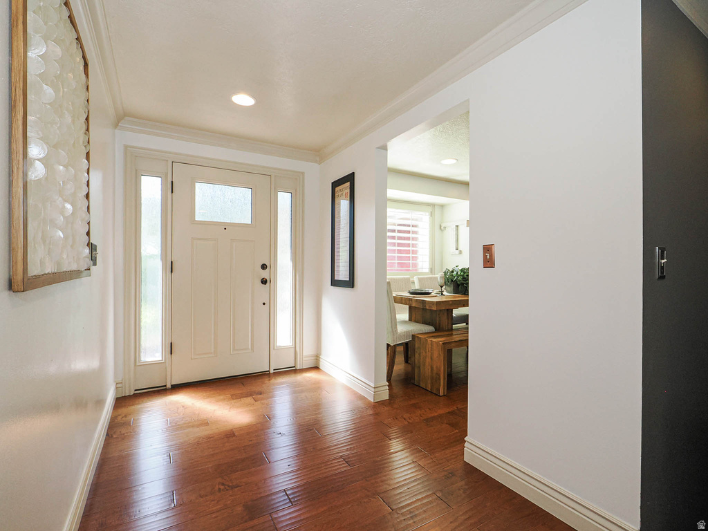 Entryway featuring wood-finish flooring, a paneled entry door with sidelights, crown molding, recessed lighting, and a wide cased opening to an adjacent dining area