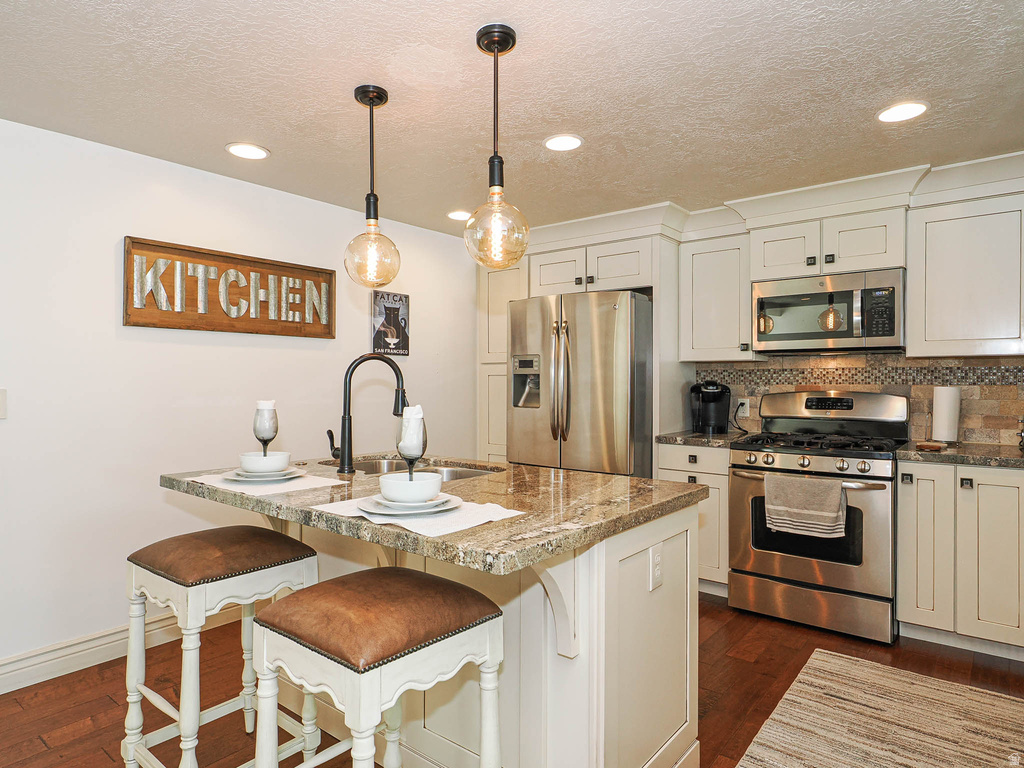 Kitchen featuring white shaker-style cabinetry, stainless steel appliances, a tile backsplash, and a central island with a sink and granite countertop