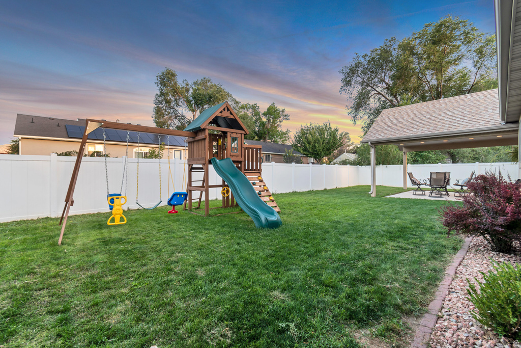 Expansive backyard featuring a covered patio, manicured lawn, and white privacy fencing