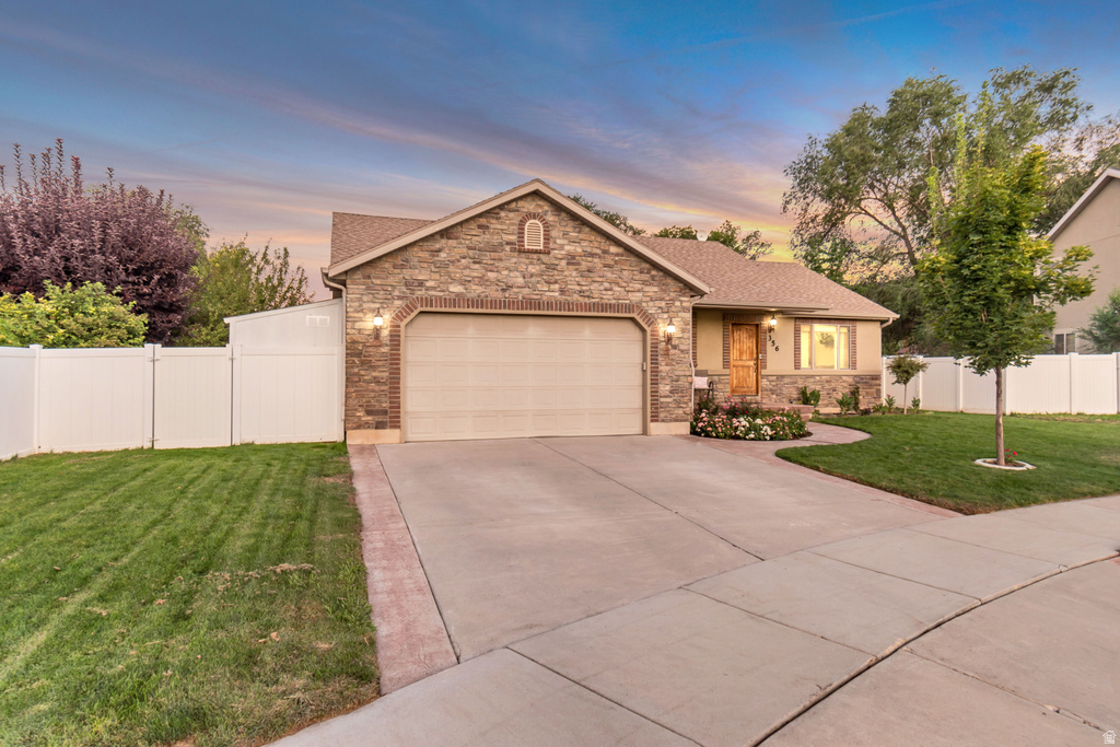 Stone-accented exterior featuring a two-car garage, concrete driveway with paver border, and a well-maintained lawn
