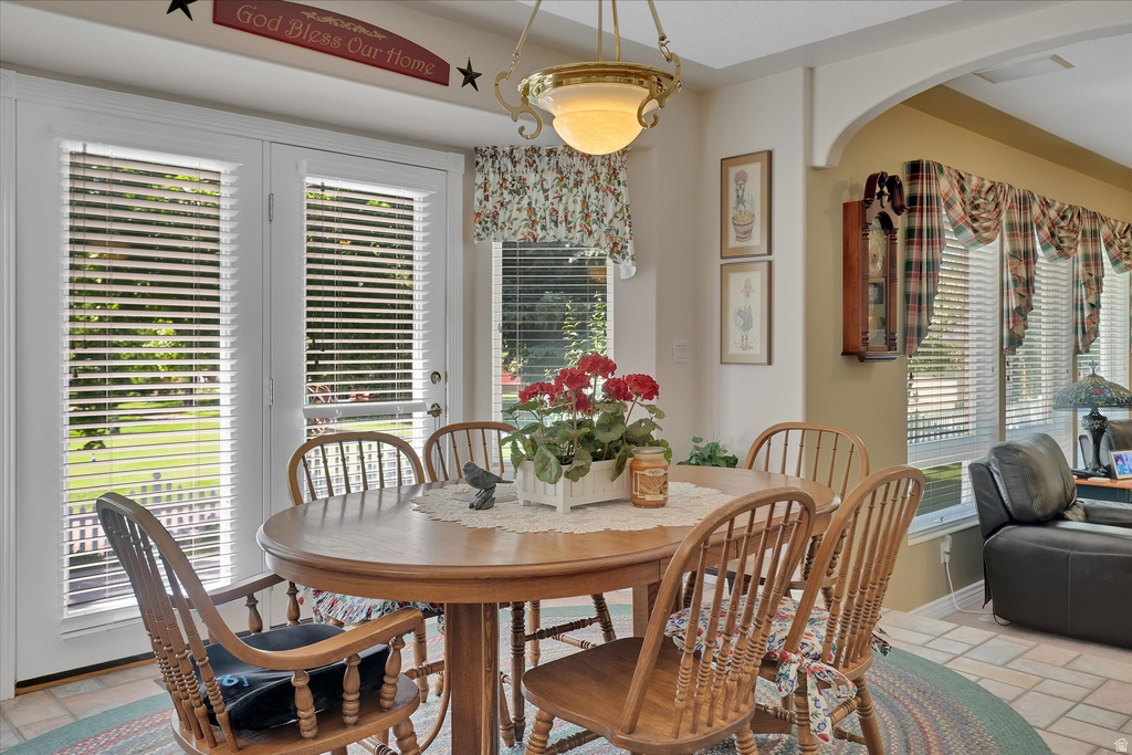 Arched entryway with a decorative light fixture, French doors with horizontal blinds, and tile flooring