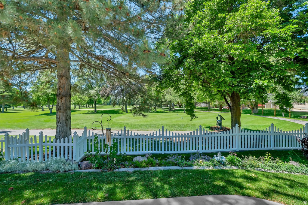 Manicured lawn with mature trees and a white picket fence, bordering a golf course