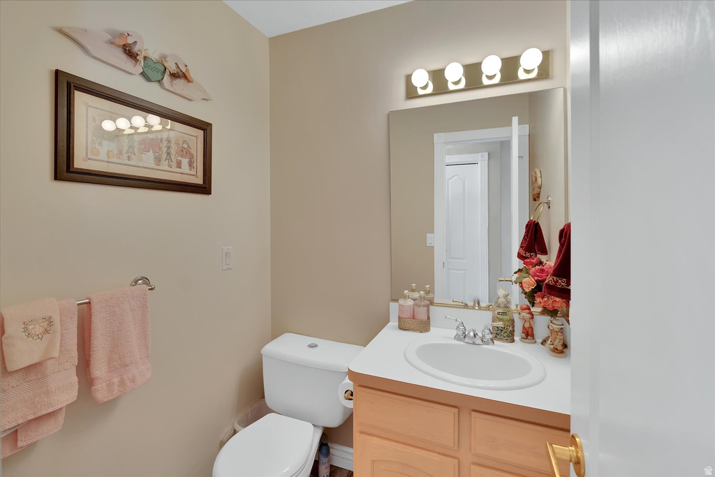 Neutral-toned powder room featuring a single vanity with an integrated sink, a large wall-mounted mirror, a four-bulb vanity light fixture, and a commode