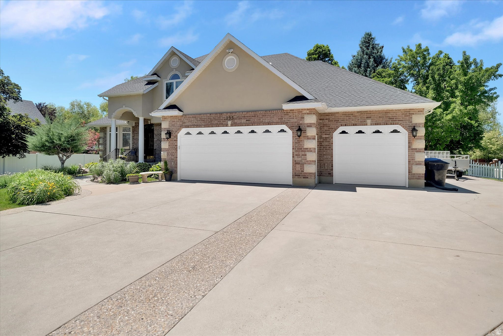 Stucco and brick exterior with a multi-car garage, featuring decorative garage doors, sconce lighting, and a paved driveway with an exposed aggregate accent strip