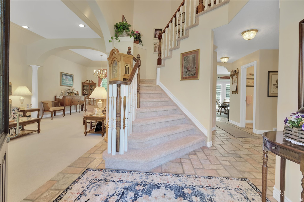 Inviting foyer with natural stone tile flooring, a carpeted staircase with wood handrail and white balusters, arched openings, and recessed lighting