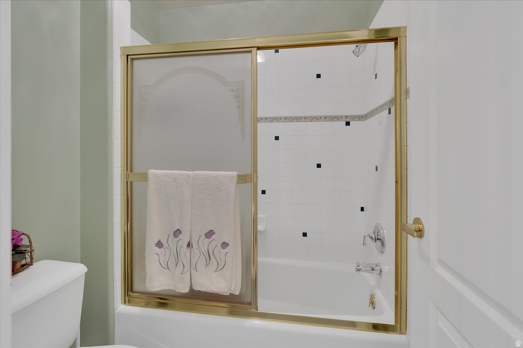 Bathtub with a gold-framed sliding glass enclosure, white subway tile surround, and decorative accent tiles