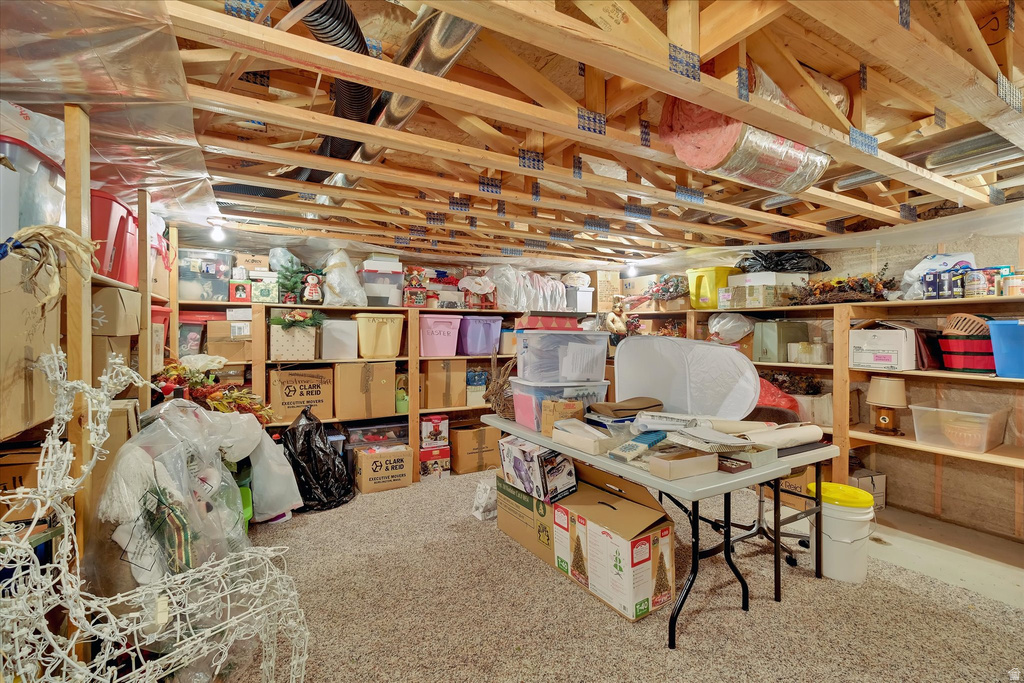 Basement space featuring exposed wood joists, concrete foundation walls, and light-colored carpeting