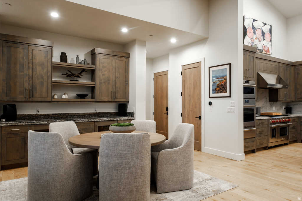 Open-concept space featuring a dining area with a round wood-finish table and upholstered chairs, alongside a kitchen with wood-finish cabinetry, stainless steel appliances, and a range hood