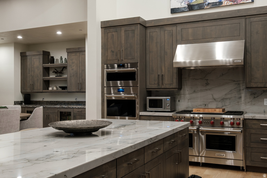 Gourmet kitchen featuring a large island with a substantial stone countertop, custom wood cabinetry, stainless steel professional-grade appliances, and a full-height stone slab backsplash