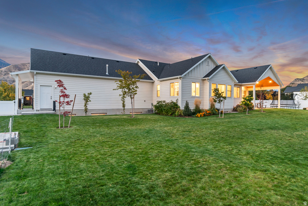 Expansive rear yard featuring a manicured lawn, established landscaping, and a covered patio with recessed lighting