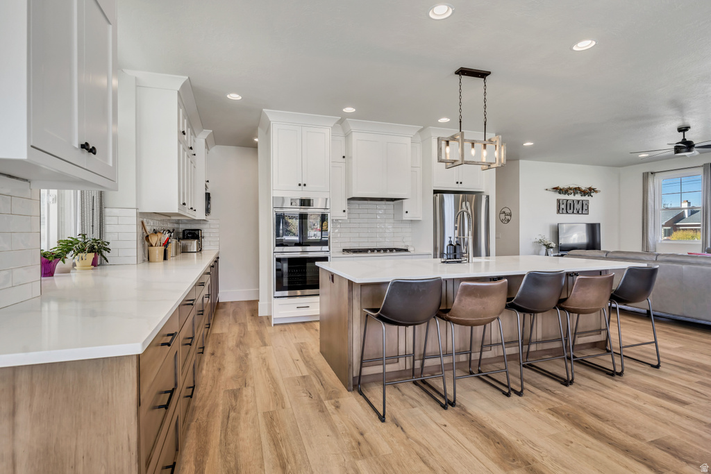 Open-concept kitchen featuring an expansive island with seating, stainless steel appliances, white subway tile backsplash, and wood-finish flooring