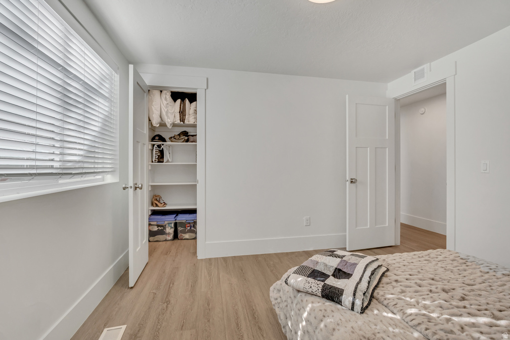 Bedroom with light wood-finish flooring, white walls, and a window with horizontal blinds