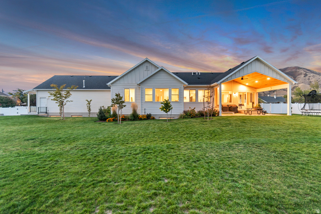 Rear elevation featuring a broad lawn, white vinyl fencing, a covered patio with a wood-paneled ceiling, and a prominent mountain backdrop