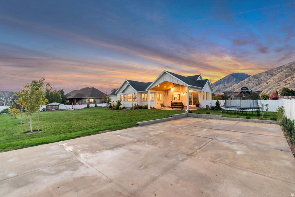 Expansive concrete patio with a spacious lawn surrounding a modern ranch-style residence featuring a covered patio with recessed lighting