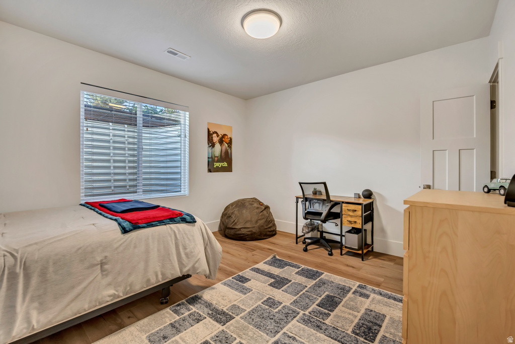 Bedroom featuring a window with blinds, wood-finish flooring, and white walls