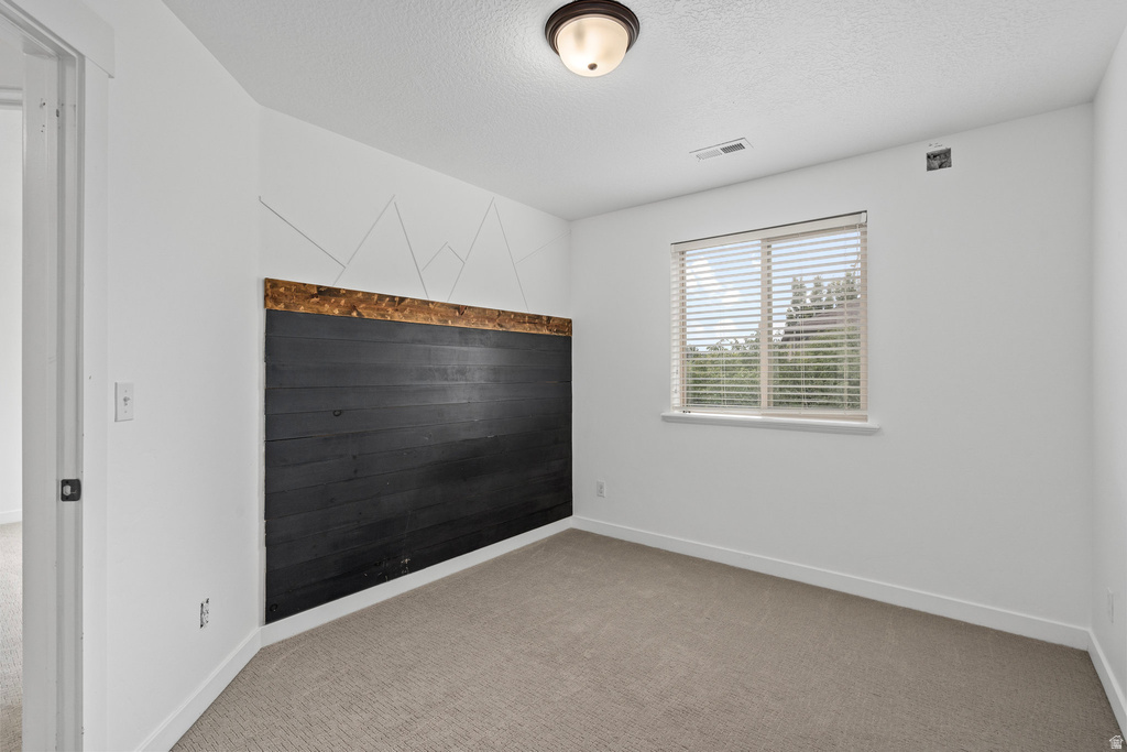 Carpeted room featuring a window with horizontal blinds, overhead flush-mount lighting, and a textured accent wall with a dark wood-finish panel and geometric detailing