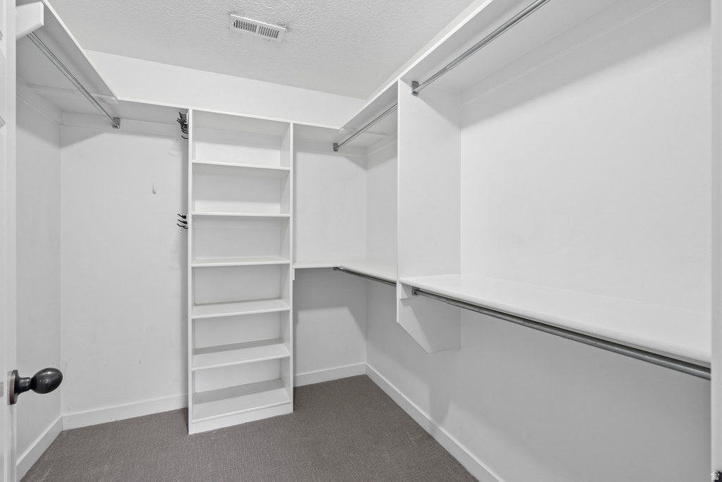 Walk-in closet featuring white built-in shelving, multiple hanging rods, and a neutral carpeted floor