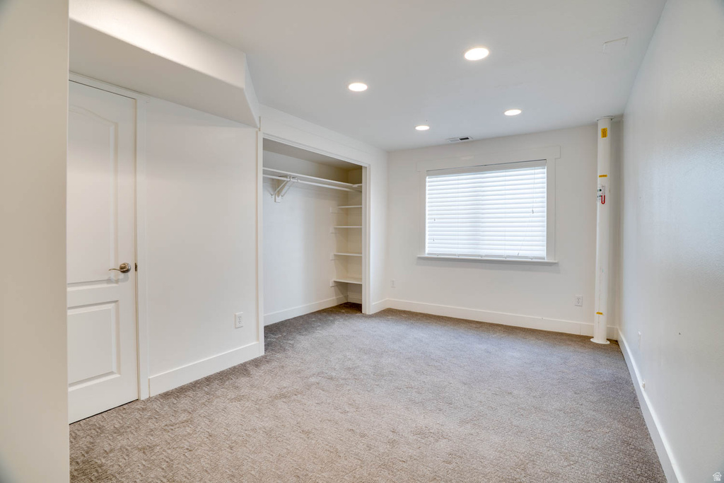 Carpeted room featuring a window with horizontal blinds, recessed lighting, a white two-panel door, and an open closet with shelving and hanging rods