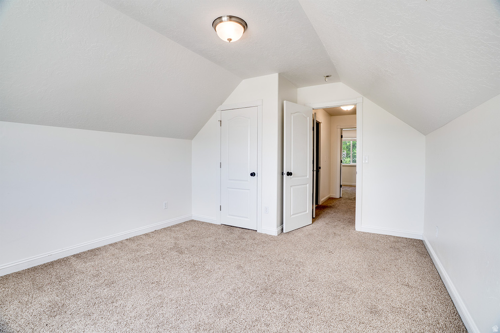 Carpeted room featuring sloped ceilings, white walls, and a semi-flush mount ceiling light