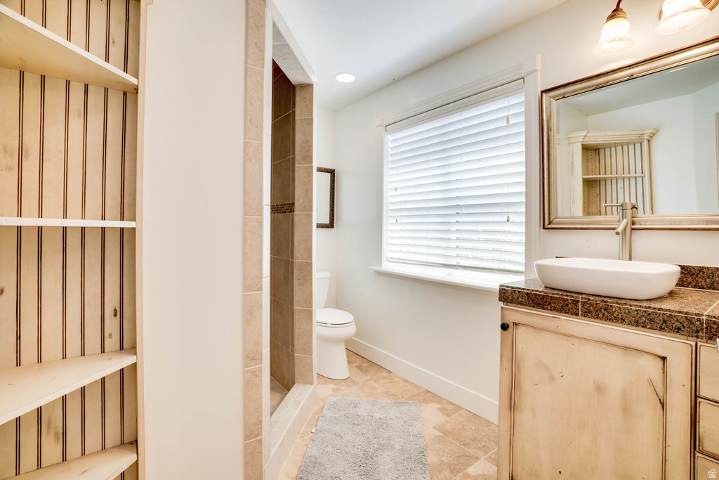 Bathroom featuring a stone tile shower, light wood vanity with a vessel sink, and a window with horizontal blinds