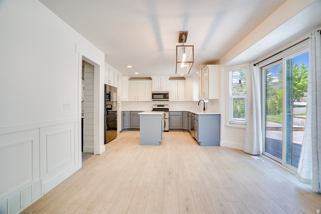 Bright kitchen and dining area featuring light wood-finish flooring, white and gray cabinetry, a central island, and modern pendant lighting