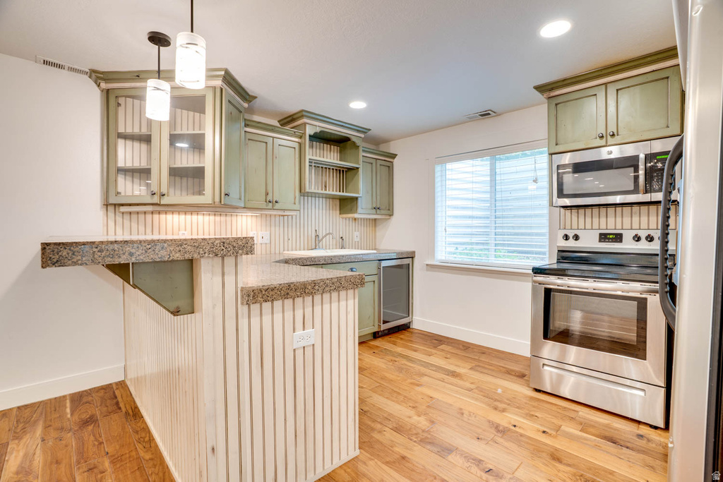 Kitchenette featuring light green cabinetry, wood-finish flooring, a stainless steel range with overhead microwave, and a breakfast bar with stone-finish countertops
