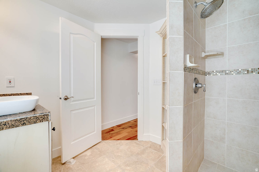 Bathroom featuring a vessel sink on a granite-look countertop vanity, tiled flooring, a walk-in shower with rain head and mosaic accent tile, and built-in shelving