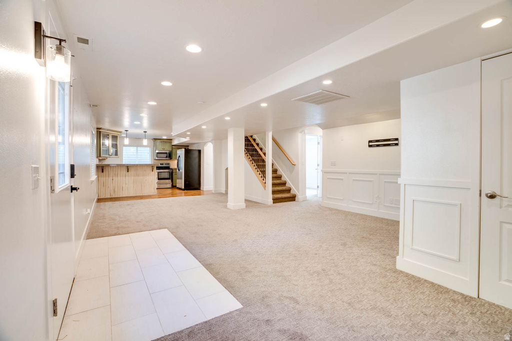 Open-concept living space featuring recessed lighting, a fully equipped kitchen with a breakfast bar, carpeted flooring, and a tiled entry