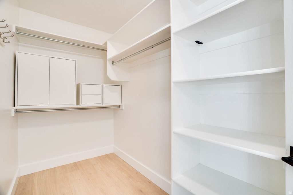 Walk-in closet featuring light wood-finish flooring, white walls, and built-in shelving