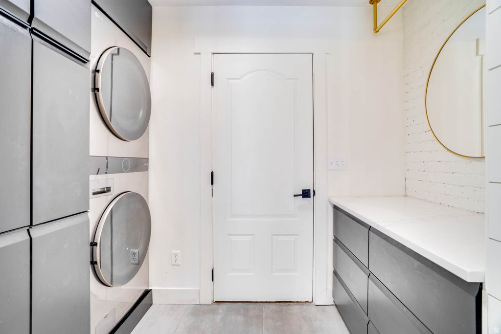 Dedicated laundry area featuring stacked front-load appliances and light wood-finish flooring